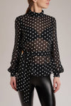 A black silk blouse with white polka-dots has blouson sleeves with buttoned cuffs and a detachable pussy-bow tie.